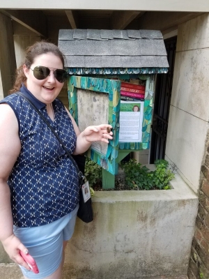 30s woman with sunglasses standing in front of a little free library